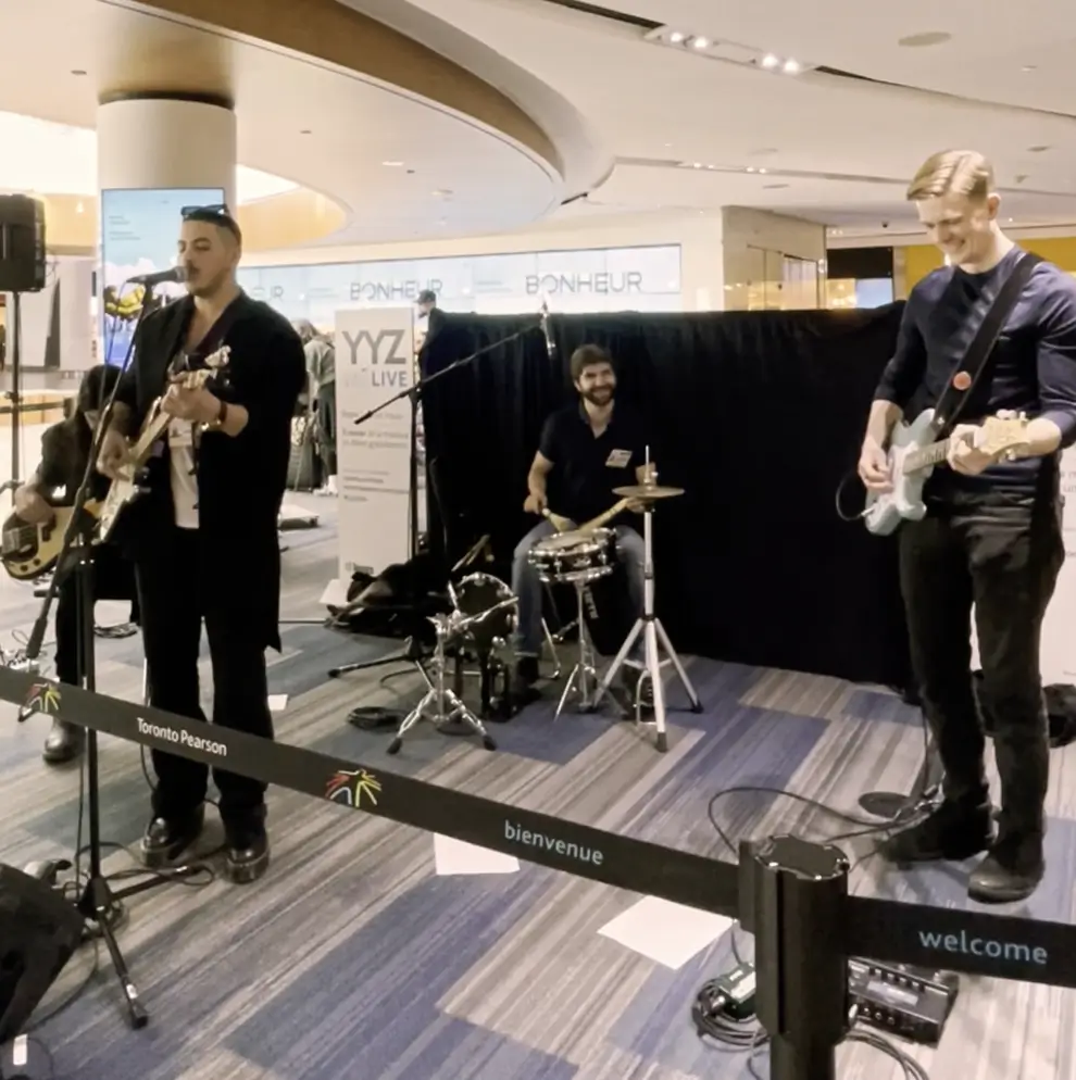 picture of Toronto based band Empire Thief. The picture is taken of the band performing at Toronto's YYZ airport. All band members are visible in the picture. Tarun Dawar (bass player), Aidan McNaughton (lead guitar player), Adam Houle (dummer), and Ahmed El Sayed (singer and guitar player)